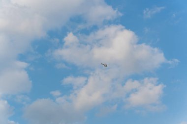 Gökyüzünde küçük bir helikopter, beyaz bulutların arasında. Güneşli bir günde çekilen.