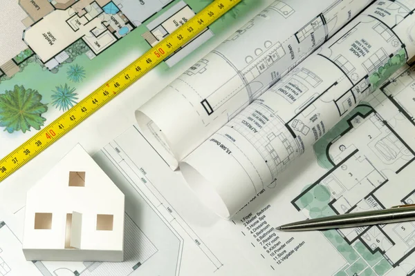 Closeup to floor plans, white paper house and measuring yellow tape. Architect drawings, expensive renovation,  building construction cost, modern design, mortgage or credit.