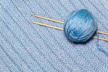 Mavi örgü kumaş arka planında örgü ipliği ve örgü iğneleri. El yapımı hobi.