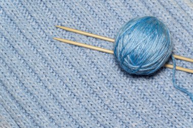 Mavi örgü kumaş arka planında örgü ipliği ve örgü iğneleri. El yapımı hobi.