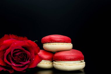 Siyah arka planda kırmızı gül ve büyük kırmızı kalp ile kırmızı badem kurabiyeleri.