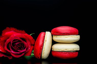 Siyah arka planda kırmızı gül ve büyük kırmızı kalp ile kırmızı badem kurabiyeleri.