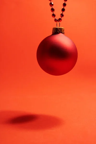 Juleball som henger på røde perler på rød bakgrunn. Totalt rødt . – stockfoto