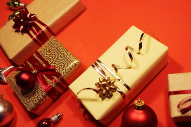 Bir sürü Noel hediyesi kutusu süslenmiş altın süslemeler, kırmızı toplar ve kırmızı arka planda fiyonklar.