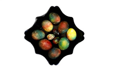 Beyaz arka planda siyah kıvırcık bir tabakta parlak renkli Paskalya yumurtaları.