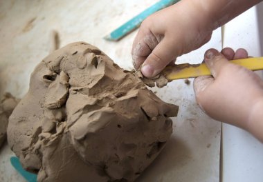Küçük bir çocuğun elleri beyaz bir masada gri bir kil parçasıyla çalışıyor. Yukarıdan görüntüle.