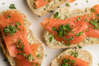 Yukarıdan çekilen beyaz tabakta duran tereyağlı ve maydanozlu alabalık sandviçleri.