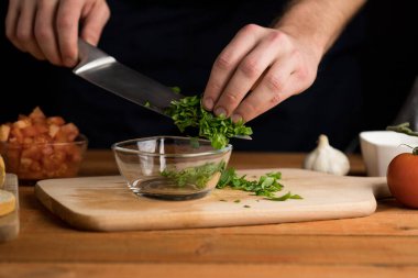 Bıçağın üzerinde doğranmış fesleğen tutan kişi, İtalyan aperatifi hazırlıyor, bruschetta, koyu arka plan, görünür eller.