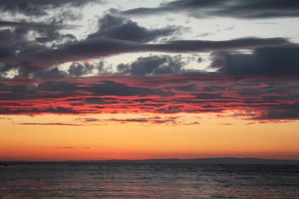 Beautiful sunset above the sea or ocean. Thick e gray clouds and the sun over the horizon. Calm sea and sunset. Photography for travel agencies, travel blogs. Nature and the sea element. Red sun sunset