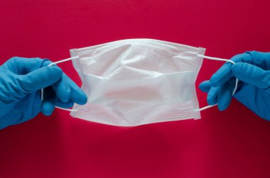 Doktorlar mavi tıbbi eldiven veriyorlar. Kırmızı arka planda solunum maskesi var. Enfeksiyonları, virüsleri, hava hastalıklarını önlemek için maske. Coronavirüs salgını konsepti, covid-19
