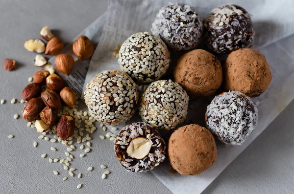 Raw vegan energy balls with hazelnut on a gray background. Natural sweets from nuts and dried fruits in coconut, cocoa and sesame seeds, close-up. Sugar-free and gluten-free sweets, raw food desserts