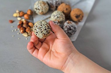 Çocuk elinde Enerji Çubukları 'nı tutuyor. Ev yapımı çiğ şeker. Karışık hurma, fındık, kurutulmuş meyve, üzerine hindistan cevizi, kakao ve susam tohumu serpiştirilmiş. Sağlıklı tatlı kavramı. Paleo, keto diyeti
