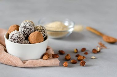 Gri arka planda fındıklı bir kasede vegan enerji topları. Hindistan cevizi, kakao ve susam tohumlu fındık ve kurutulmuş meyvelerin doğal tatlısı. Yakın plan. Şekersiz çiğ yiyecek konsepti