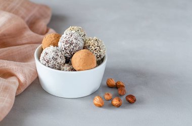 Gri arka planda fındıklı bir kasede vegan enerji topları. Hindistan cevizi, kakao ve susam tohumlu fındık ve kurutulmuş meyvelerin doğal tatlısı. Yakın plan. Şekersiz çiğ yiyecek konsepti