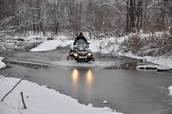 Een Atv op wielen steekt een bevroren rivier over die ijs breekt. — Stockfoto