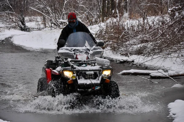 Een Atv op wielen steekt een bevroren rivier over die ijs breekt. — Stockfoto