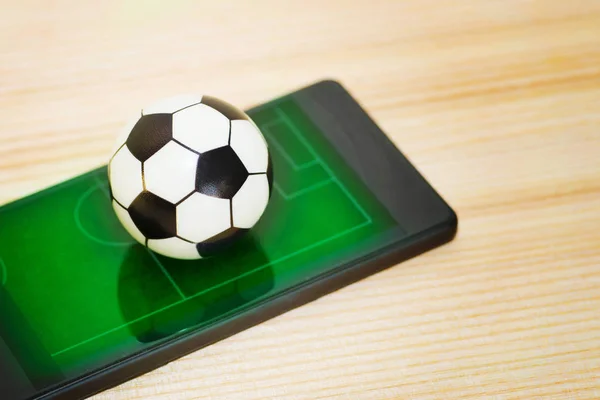 Un ballon de football jouet sur un smartphone avec une photo d'un terrain vert. Concept du jeu de football . — Photo