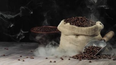 Kahve çekirdeklerinin bileşimi. Ahşap masa arkaplanı kahve çekirdekleri, kase ve kokulu kahve çekirdekleri ile süslenmiş. Buhar ahşap masadaki tahıllardan geliyor. Ağır çekim. 4k