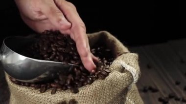 Kahve çekirdeklerinin bileşimi. Ahşap masa arkaplanı kahve çekirdekleri, kase ve kokulu kahve çekirdekleri ile süslenmiş. Kahve çekirdekleri kepçeden kaseye dökülür. 4k