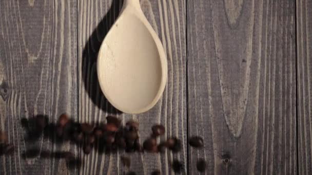 木製の背景にある木製のスプーンから焙煎されたコーヒー豆が吹き飛ばされます フレッシュブローコーヒー豆の香り スローモーション — ストック動画