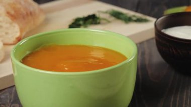 Kremalı balkabağı çorbası. Şef süslemeli ahşap masada yeşil bir kaseye kremalı balkabağı çorbası koyar. Kapatın. 4k.