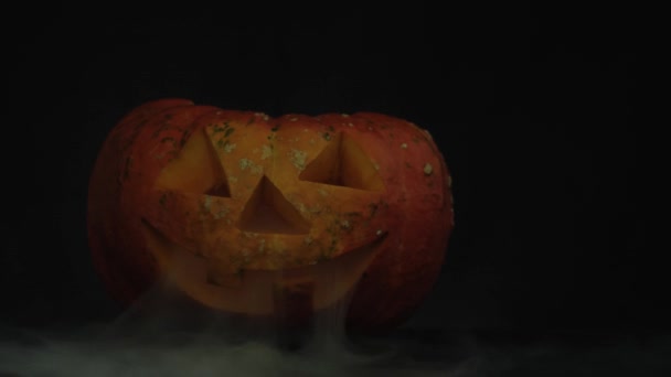 Citrouille d'Halloween sculptée Jack-o-lanterne avec des bougies sur une table sombre avec de la fumée blanche. La lumière est allumée. Au ralenti. Tir rapproché. 4K .