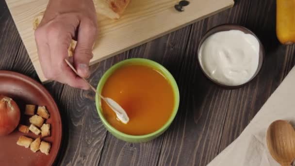 クリーミーなカボチャのスープ料理 シェフは飾り木のテーブルの上の緑のボウルにサワークリームをカボチャのスープに入れます最上階だ4K — ストック動画