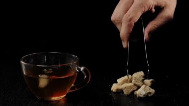Çay seremonisi. El kahverengi şekeri alır ve siyah arka planda siyah bir masaya şeffaf bir kupa koyar. Modern soğuk Çin töreni.