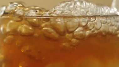 Çay seremonisi. Köpüklü köpüklerle buz küpleri, limon dilimleri ve parlak arka planda duran nane şekerleriyle şeffaf bir bardağa dönüşür. Modern soğuk Çin töreni. Kapatın. Yan görünüm