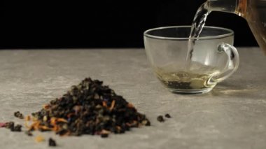 Çay seremonisi. Yeşil çay şeffaf bir fincana dökülüyor ve yeşil çay yaprakları yığınının yanındaki siyah arka planda duruyor.