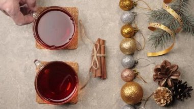 Yeni yıl ve Noel süsü. Biraz kozalak, Noel ağacının dalları, gümüş dokuda tarçın çubukları, kurdeleler ve çiçekler. El, masadan yılbaşı çayıyla bardağı alır. Üst görünüm