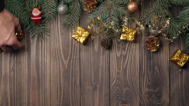 新年とクリスマスの装飾 手はいくつかのプレゼント クリスマスボール 松のコーンと木製のテーブルの上にクリスマスツリーの枝の近くにサンタクロースの小さなおもちゃを置きます トップ表示 — ストック動画
