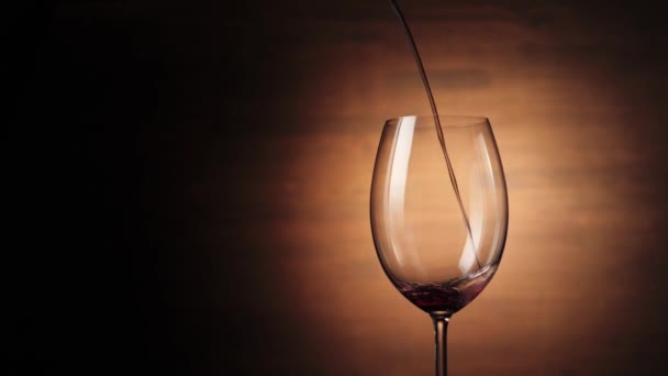 Luxusní červené víno. Ruka nalévá lahodné víno z gejzíru ve sklenici vína na hnědém pozadí. Růžové víno z lahodných červených hroznů nalévajících se z láhve do poháru. Zpomalený pohyb