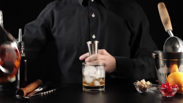 altmodischer Cocktail. Barkeeper nimmt einen Jigger, gießt Bourbon aus einer runden Flasche hinein und gießt den Inhalt in das Rockglas. iba offizieller Cocktail. Weitschuss