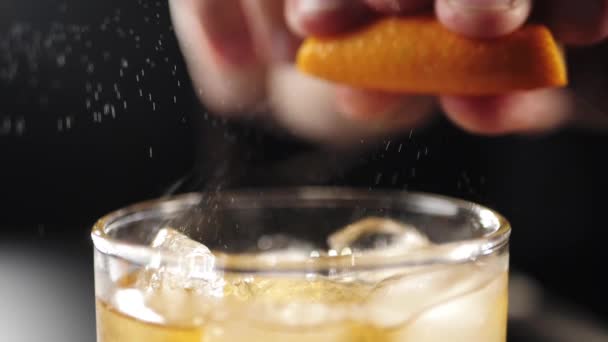 Old Fashioned cocktail. Bartender sprinkles on the edges of the rocks glass by droplets from the zest of orange to enhance the taste of the cocktail. IBA official cocktail. Close up