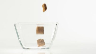 Taze sağlıklı yiyecekler. Çikolatalı gevrek pedleri beyaz arka planda şeffaf bir kare kaseye düşer. Sağlıklı kahvaltı, temiz yemek, diyet, detoks, vejetaryen, vejetaryen yemeği. Yan görünüm