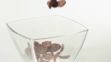 Taze sağlıklı yiyecekler. Çikolatalı gevrek taneleri beyaz arka planda şeffaf bir kare kaseye düşer. Sağlıklı kahvaltı, temiz yemek, diyet, detoks, vejetaryen, vejetaryen yemeği. Üst görünüm