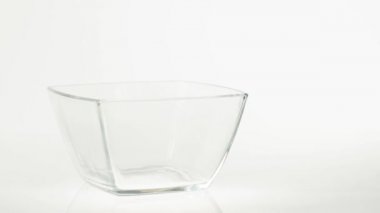 Taze sağlıklı yiyecekler. Çikolatalı gevrek topları beyaz arka planda şeffaf bir kare kaseye düşer. Sağlıklı kahvaltı, temiz yemek, diyet, detoks, vejetaryen, vejetaryen yemeği. Yan görünüm