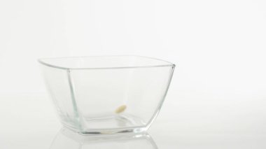 Taze sağlıklı yiyecekler. Sarı mısır gevrekleri beyaz arka planda şeffaf bir kare kaseye düşer. Sağlıklı kahvaltı, temiz yemek, diyet, detoks, vejetaryen, vejetaryen yemeği. Yan görünüm