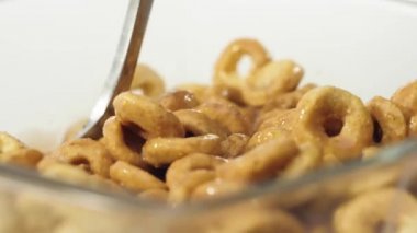 Taze sağlıklı yiyecekler. Kaşık, beyaz arka planda şeffaf kaseden çikolatalı sütle sarı mısır gevreğini yakalar. Sağlıklı kahvaltı, temiz yemek, diyet, vejetaryen yemek kavramı. Kapat.