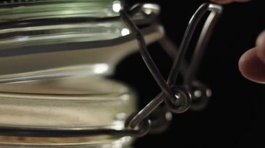 Taze sağlıklı yiyecekler. Bir kavanozu ahşap masada yulaf gevreğiyle kapatır ve siyah arka plandaki bir bardak sütün yakınındaki yeşil bir kaseye yulaf gevreği döker. Sağlıklı kahvaltı kavramı, temiz yemek.