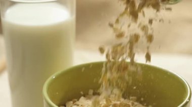 Taze sağlıklı yiyecekler. Sarı yulaf gevrekleri, beyaz sütlü bardağın yanındaki yeşil yuvarlak bir kaseye düşer. Sağlıklı kahvaltı, temiz yemek, diyet, detoks, vejetaryen, vejetaryen yemeği. Yan görünüm