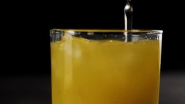 Barmen kaşığı taze portakal suyuyla buz karıştıran uzun bir bardağın içinde siyah arka planda.