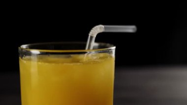 Kokteyl pipetinin taze portakal suyuna düşüşünü uzun bir bardakta buzla siyah arka plana düşüşünü.