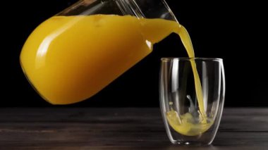 Kızın elini sürahi içerken ve portakal suyunu siyah arkaplana karşı ahşap masada çift duvarlı camda buzla gözlerken çekeceğiz.