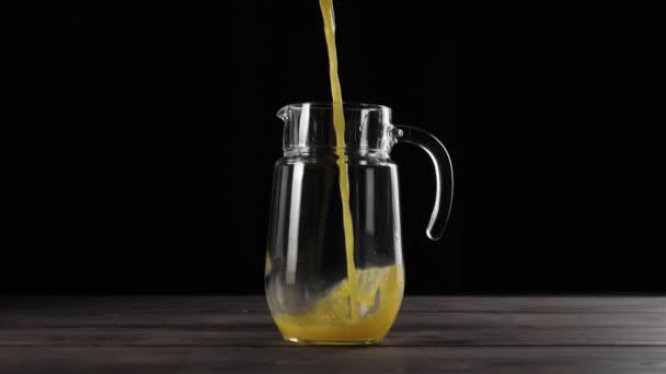 一大杯新鲜橙汁倒入透明的酒瓶中 倒在一张黑色背景的木制桌子上 — 图库视频影像