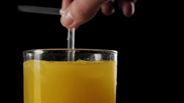 女孩的手与鸡尾酒稻草搅拌冰块与新鲜橙汁在一个黑色背景的高玻璃杯侧面视图 — 图库视频影像