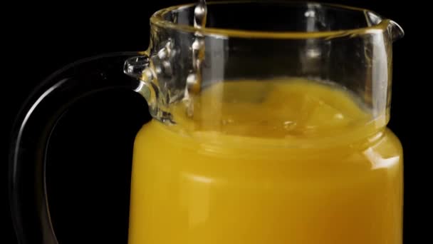 黒を背景にスローモーションでデカンターで新鮮なオレンジジュースとアイスキューブを攪拌バーテンダースプーンのクローズアップ — ストック動画
