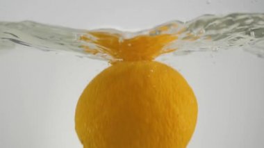 Taze bir portakal suya dökülüyor ve ışık arka planına karşı kabarcıklar oluşuyor. Sağlıklı ve temiz yemek, diyet, detoks, vejetaryen, vejetaryen yemek kavramı. Geniş açı