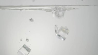 Su birikintileri ve kabarcıklarla suya düşen buz küpleri, arka planda ışığa karşı. Sağlıklı ve temiz yemek, diyet, detoks, vejetaryen, vejetaryen yemek kavramı. Geniş açı